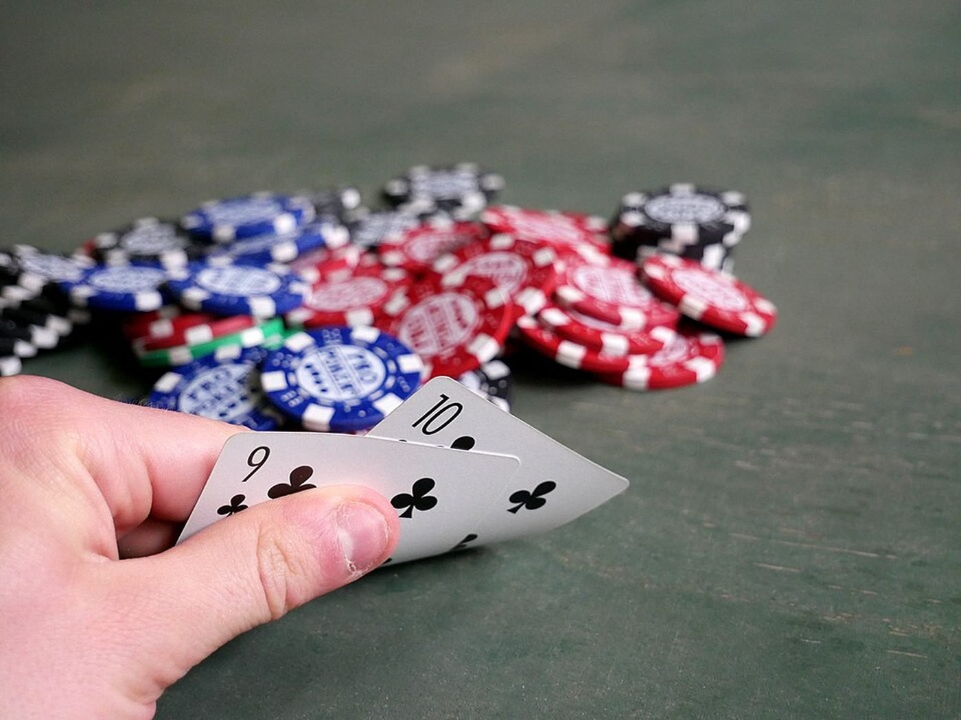 Main de poker tenue au-dessus d’un tas de jetons bleus, rouges et blancs